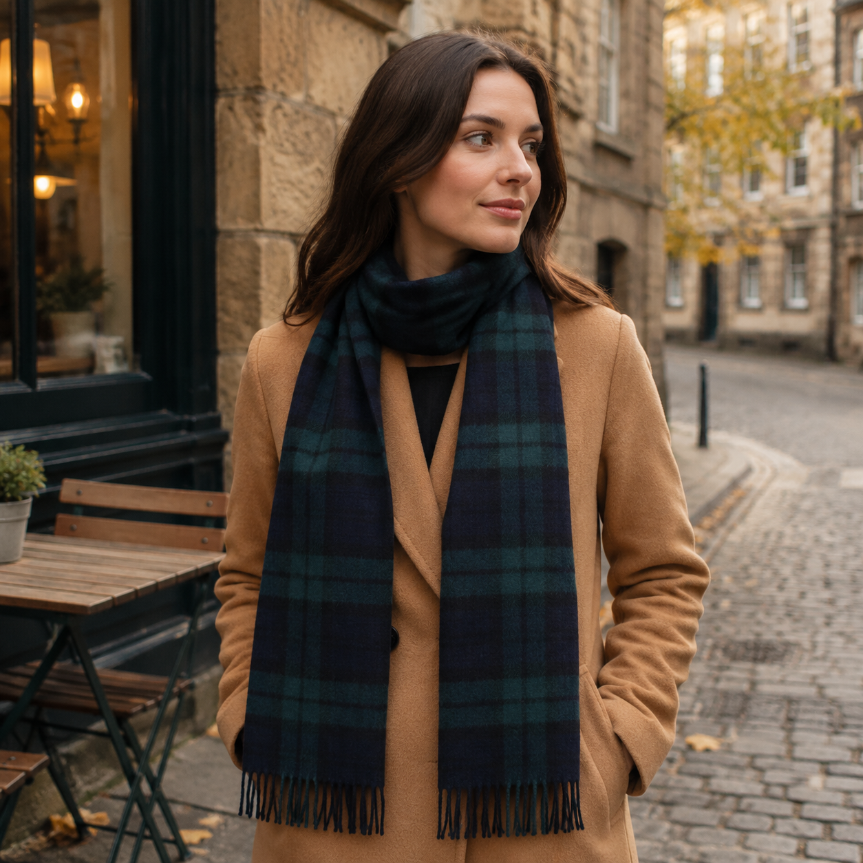 Woman wearing a Black Watch tartan lambswool scarf with a camel coat on an autumn city street