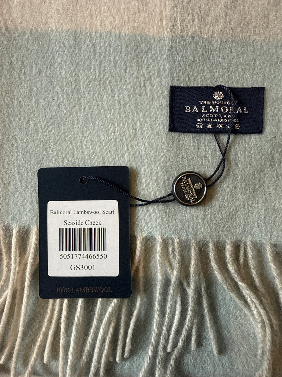 Close-up of The House of Balmoral Seaside Check 100% lambswool scarf showing the branded label and soft fringe