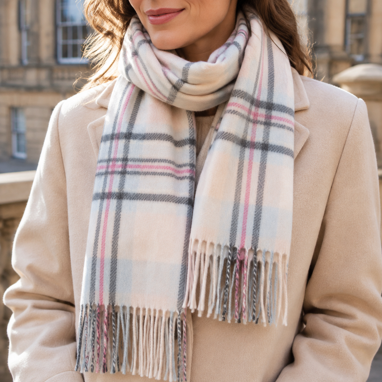 Woman wearing a cream and pale-blue checked lambswool scarf with grey and pink stripes and a beige coat
